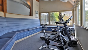 Une salle de sport avec un banc bleu, un vélo de spinning et un tapis de course.
