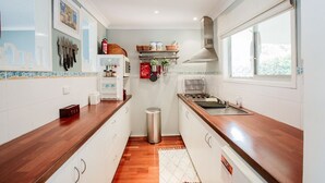 A compact kitchen with wooden countertops, white cabinets, a stainless steel trash bin, and a window providing natural light.