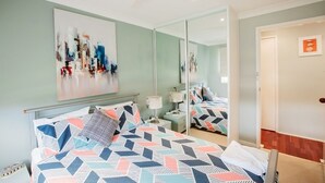 A bedroom with a bed, a nightstand, a lamp, and a large mirror.