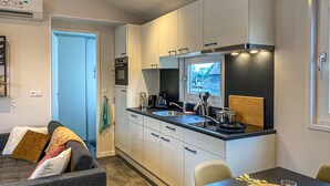 Una cocina compacta con horno integrado, microondas y pileta. Hay una mesa de comedor con sillas y un ventanal pequeño sobre la pileta.