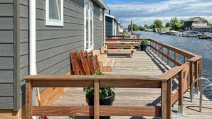 Terraza de madera con bancos y plantas en macetas, con vista a un puerto deportivo y embarcaciones.