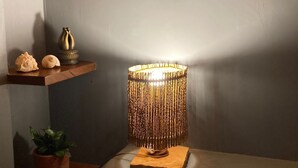 Un rincón con una pared texturizada, una lámpara decorativa, un pequeño estante con conchas, una planta en maceta y una estatua.