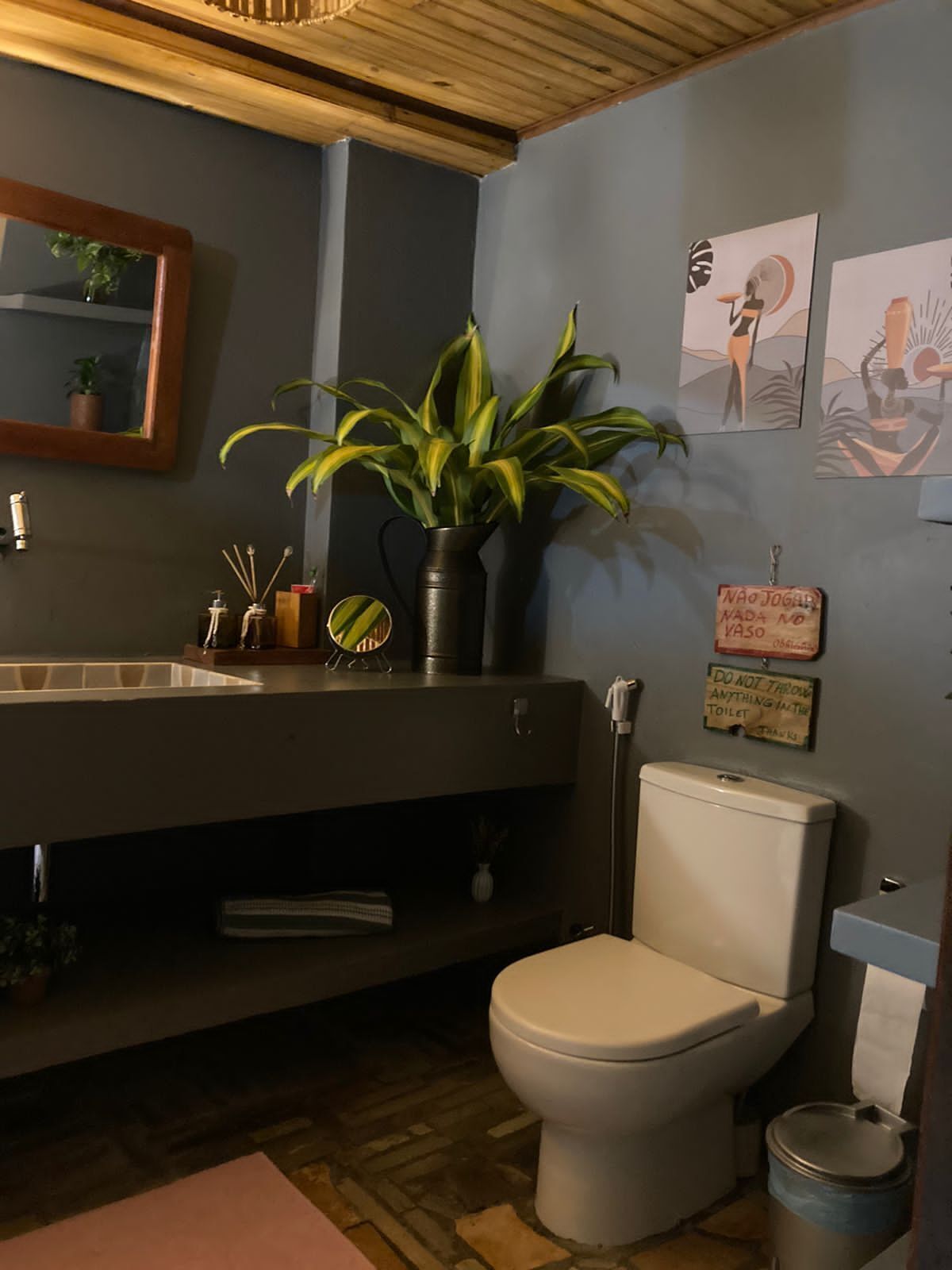 Une salle de bain avec un plafond en bois, un lavabo avec un miroir, des toilettes et une poubelle.
