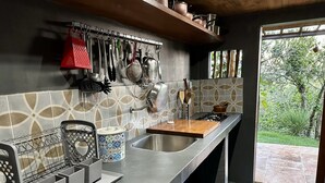 Cocina moderna con encimera de acero inoxidable, un colgador para ollas y una ventana con vistas a zonas verdes.