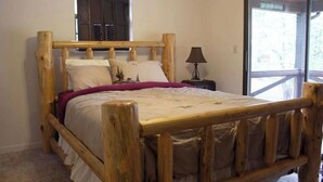 Un letto di legno con testiera, un comodino con una lampada e una finestra con vista sugli alberi.
