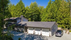 A two-story house with a garage, surrounded by dense green trees. - Immaculately Clean 2-Bedroom Suite in Serene Rural Setting (Reg # H706197976) (Langley)