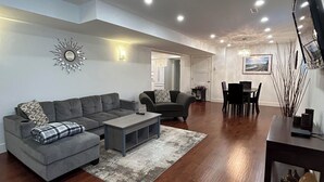 A spacious living room with a grey sectional sofa, a coffee table, and a dining area with a table and chairs. - Immaculately Clean 2-Bedroom Suite in Serene Rural Setting (Reg # H706197976) (Langley)