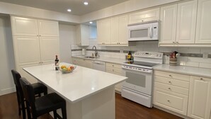 A modern kitchen with white cabinetry, a central island, black bar stools, a built-in oven, and a microwave. - Immaculately Clean 2-Bedroom Suite in Serene Rural Setting (Reg # H706197976) (Langley)