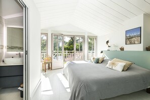 A bedroom with a large bed, a bathroom with a sink, and a view of the outdoors through glass doors.