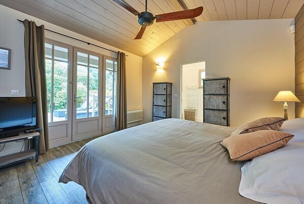 Un dormitorio con cama, ventilador de techo, televisor y ventana con cortinas.
