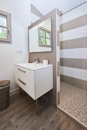 Un baño moderno con un tocador blanco, un espejo grande y una ducha con baldosas a rayas.