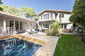 A two-story house with a swimming pool, outdoor seating, and a well-maintained lawn.