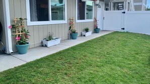 Uma casa com varanda coberta, vasos de plantas e um pequeno jardim.