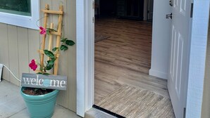 Uma porta que dá para um quarto com piso de madeira, tapete de boas-vindas e um vaso com flores.