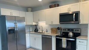 Uma cozinha moderna com eletrodomésticos de aço inoxidável, armários brancos e painel de azulejos.