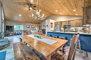 A spacious living area with a large wooden dining table, a kitchen with modern appliances, and a ceiling fan.