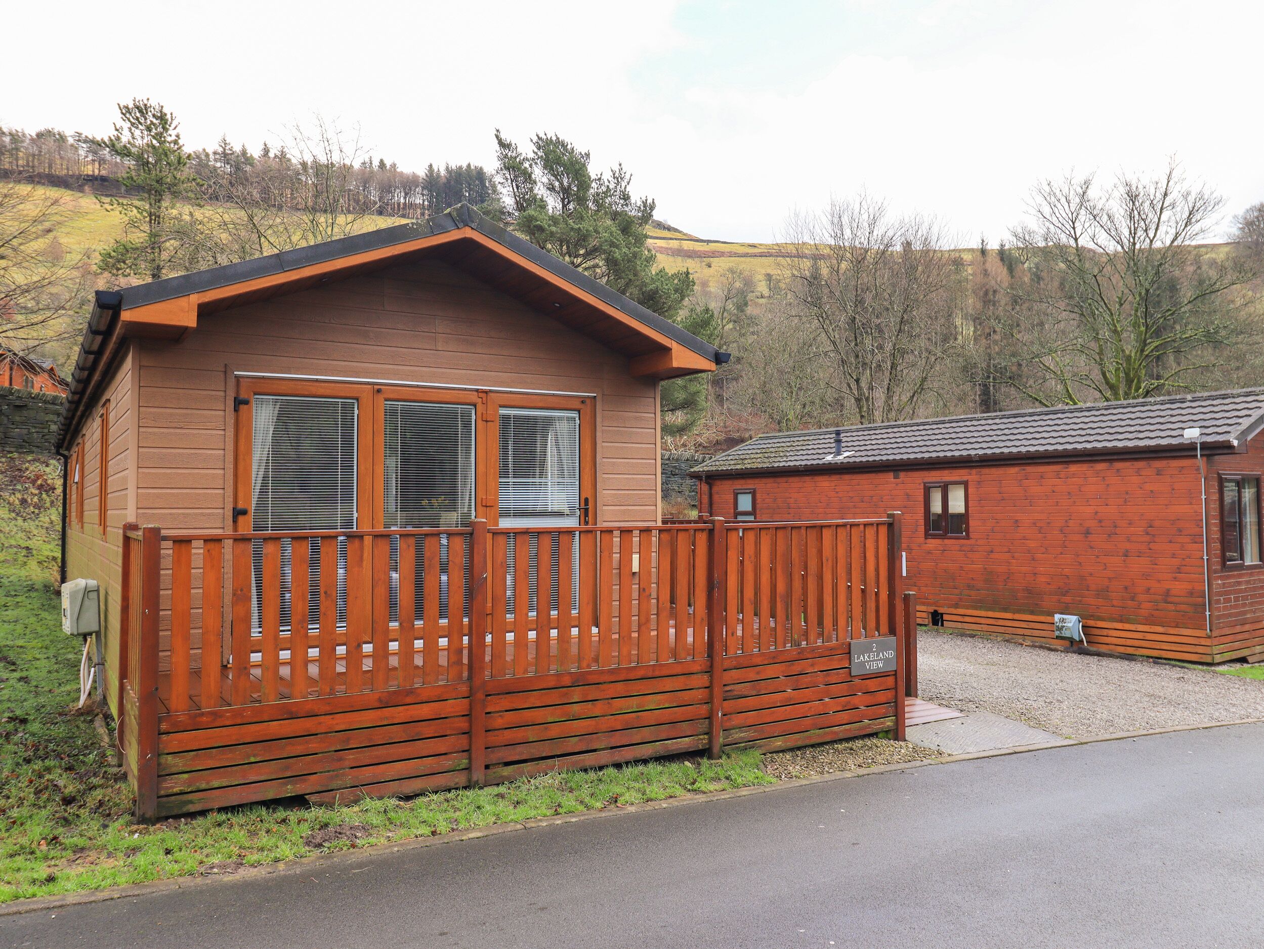 Eine Holzhütte mit umzäunter Terrasse, einem kleinen Anbau und Blick auf die umliegende Landschaft.