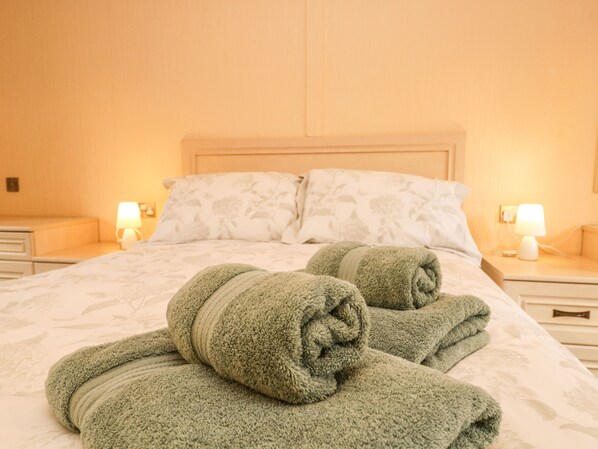 A neatly made bed with two rolled towels, a wooden headboard, and bedside lamps on a nightstand. - Damson Lodge (Windermere)