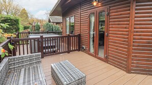 Une cabane en bois dotée d’une terrasse, de meubles de jardin et d’une porte d’entrée en verre.