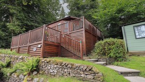 Une cabane en bois avec un mur de soutènement en pierre et un petit escalier en pierre menant à une terrasse.