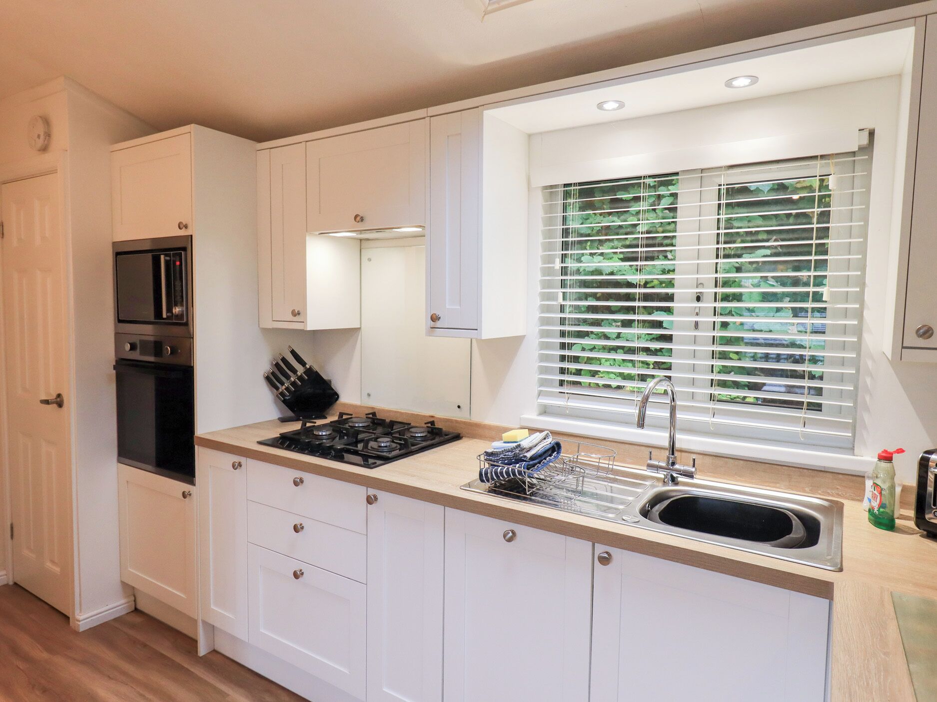 A compact kitchen with white cabinets, a built-in microwave, a gas stove, and a window with blinds.