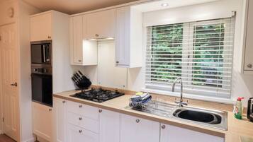 A compact kitchen with white cabinets, a built-in microwave, a gas stove, and a window with blinds.