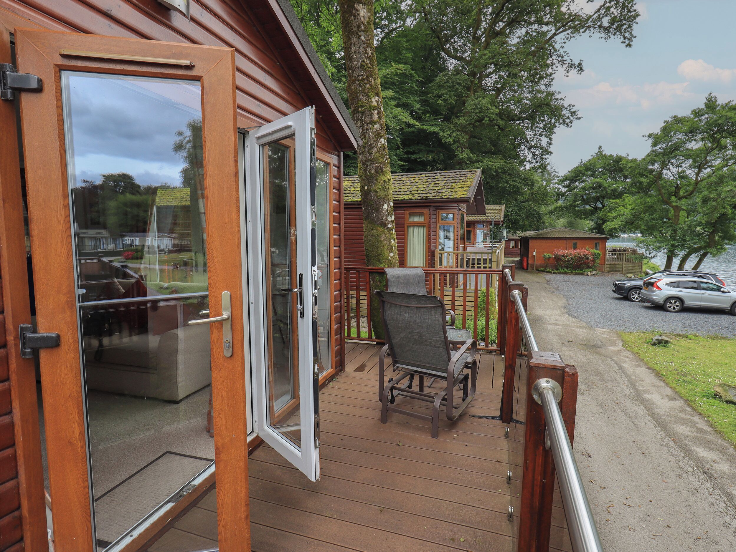 A wooden cabin with a deck, a chair, and a car parked outside.