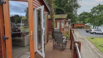 A wooden cabin with a deck, a chair, and a car parked outside.