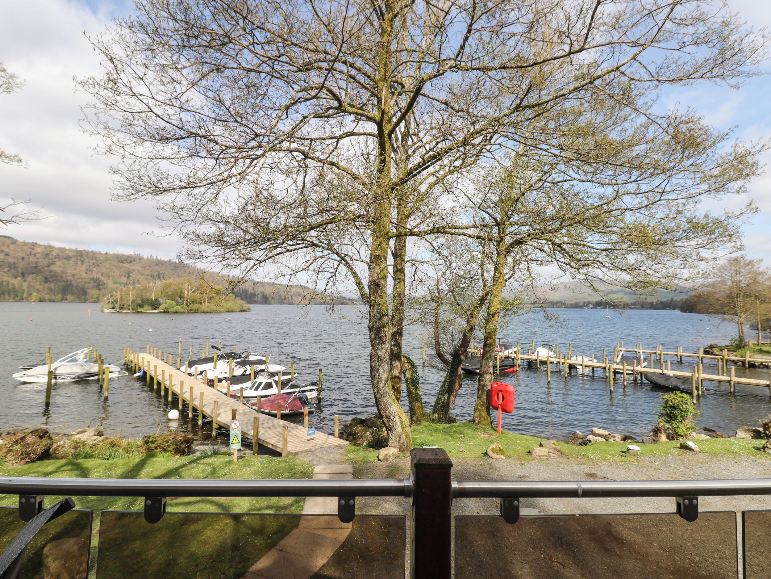 A lakeside view with docked boats, a wooden pier, and a large tree in the foreground.