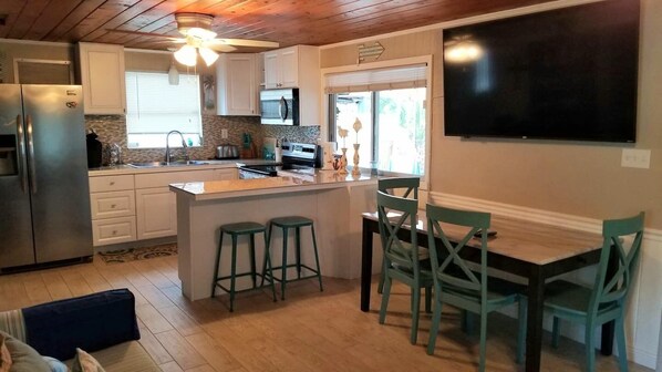 A kitchen with a refrigerator, stove, and sink. There is a dining area with a table and chairs.