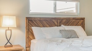 A neatly made bed with white linens and a wooden headboard, a bedside lamp, and a window above the bed.