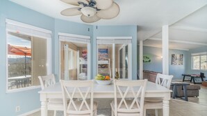 A dining area with a white table and chairs, a ceiling fan, and a view of the outdoors through large windows.