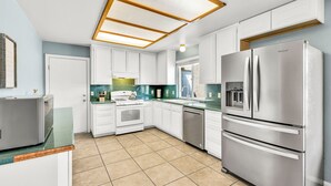 A modern kitchen with white cabinets, stainless steel appliances, and a large window.