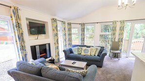 A living room with two sofas, a coffee table, a TV mounted on the wall, and a fireplace. - Forest Pines Lodge (Windermere)