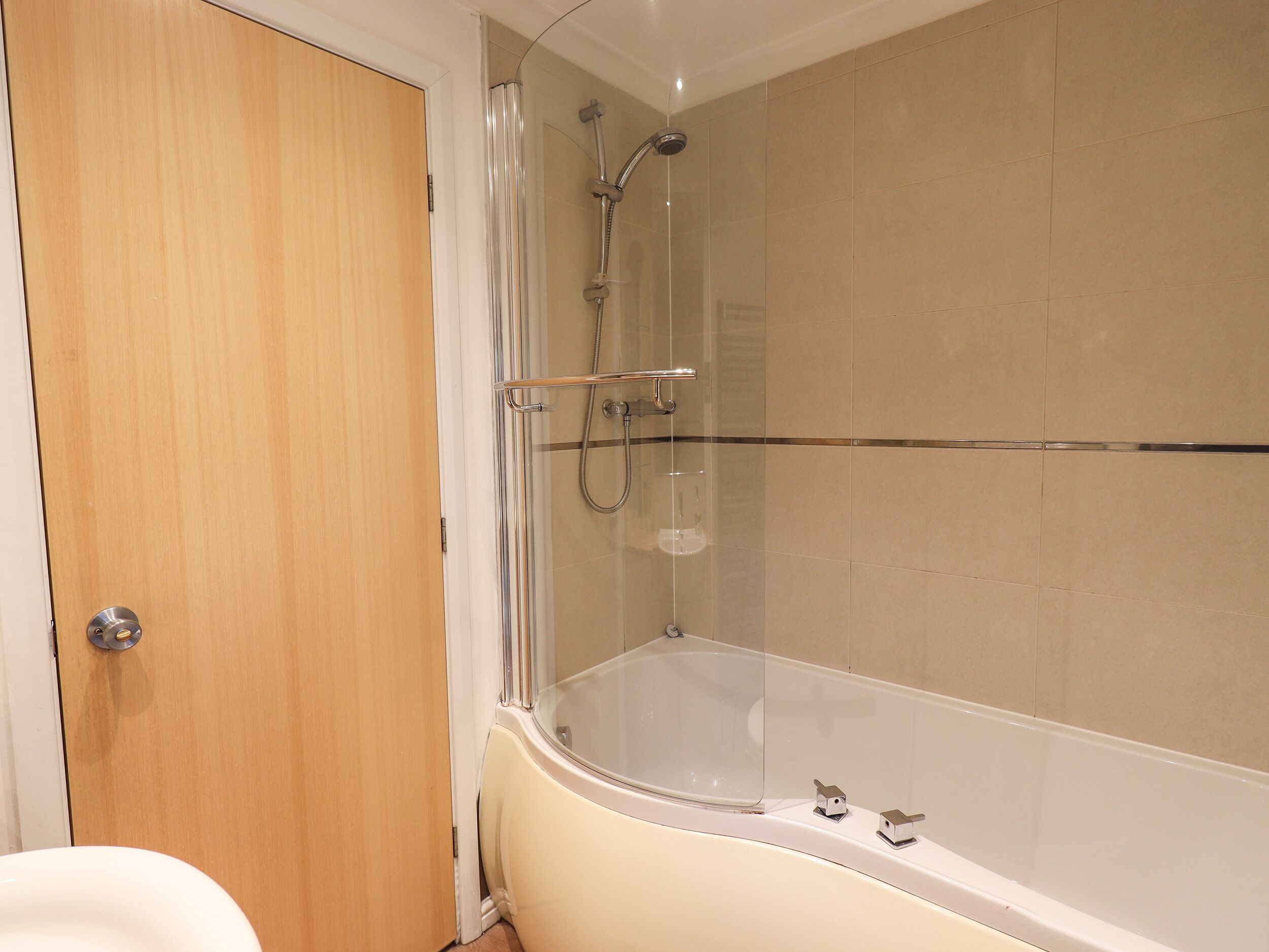 Un baño con bañera, ducha de vidrio y puerta de madera.