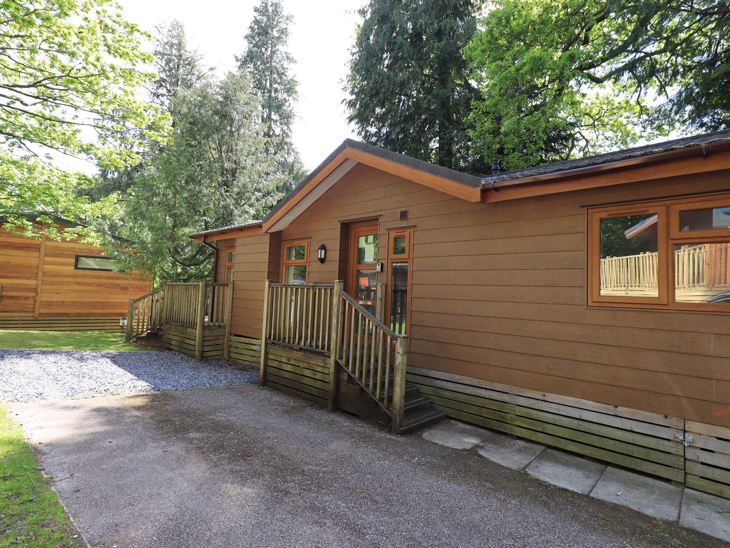 A wooden cabin with a porch, a staircase, and a gravel driveway.