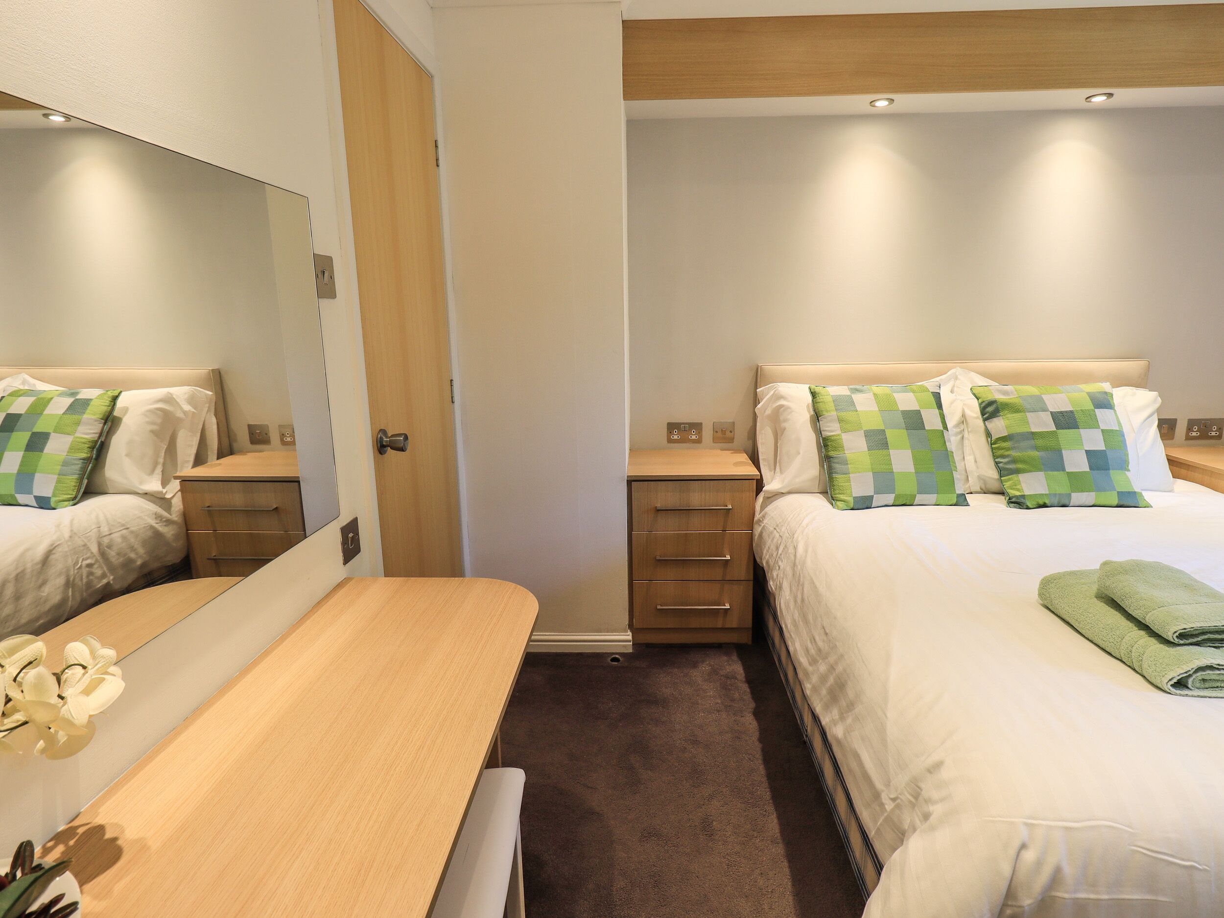A hotel room with two beds, a desk, and a mirror.