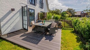 A patio with a table and chairs, a wooden deck, and a white brick wall. - Villa Maybach, Whg. 5 Metropol - Villa Maybach (Sylt)