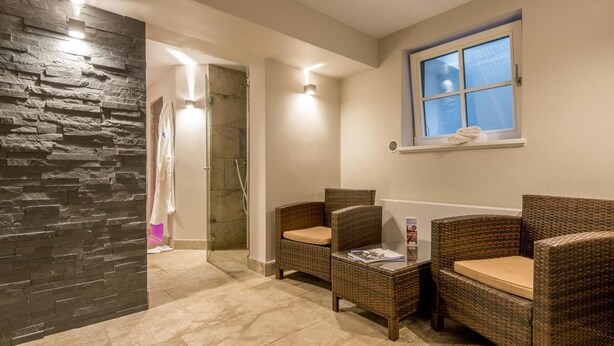 A spa area with wicker chairs, a glass table, a stone wall, and a shower room. - Villa Maybach, Whg. 5 Metropol - Villa Maybach (Sylt)