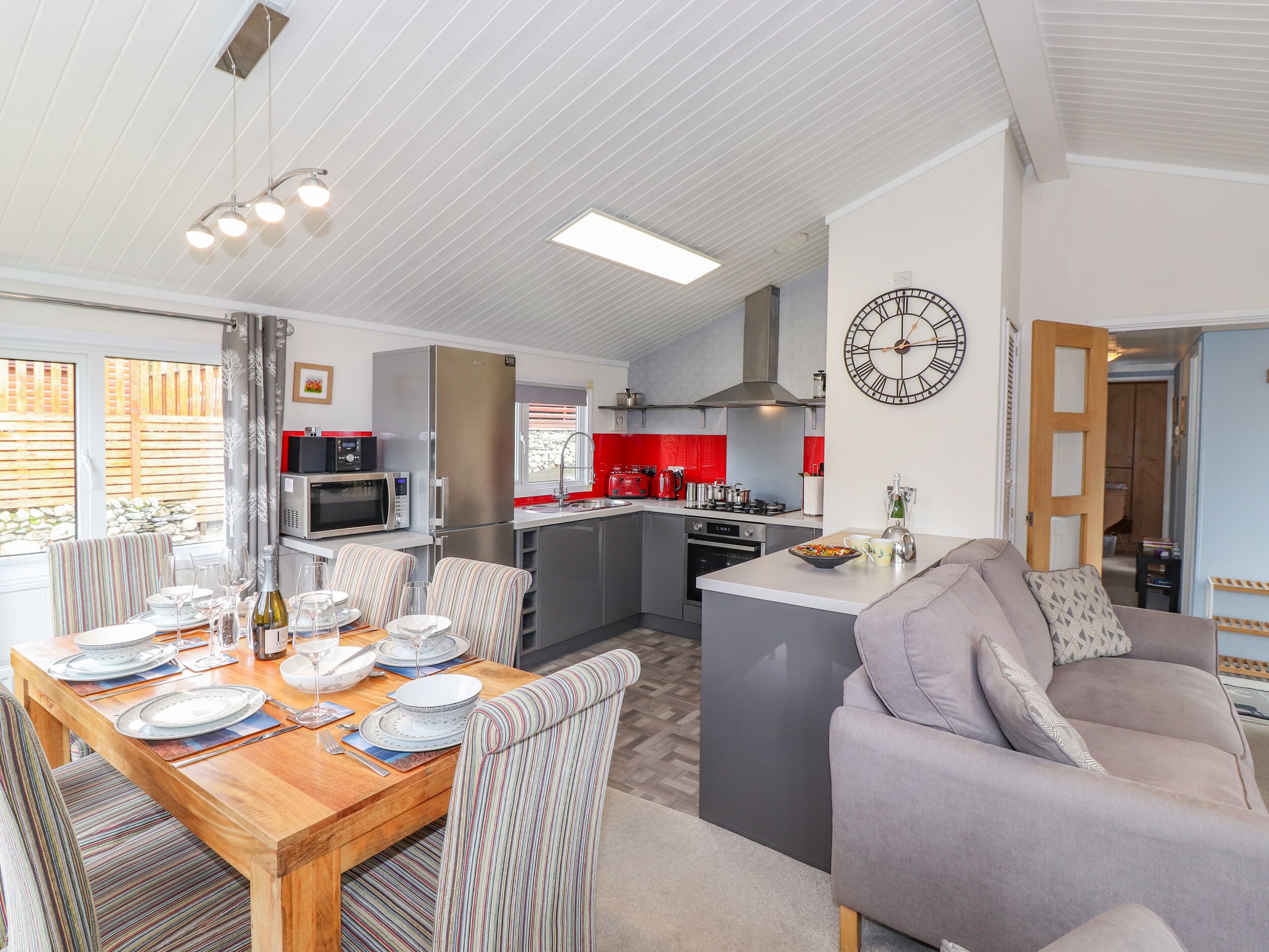 A modern kitchen with a central island, a dining area with striped chairs, and a living area with a sofa.