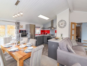 A modern kitchen with a central island, a dining area with striped chairs, and a living area with a sofa.