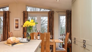 A kitchen with a wooden table, chairs, a bread loaf, a wine bottle, and a vase of flowers. - Wainwright Lodge (Windermere)