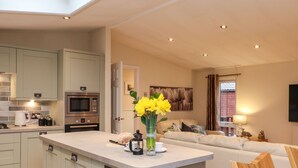 A modern kitchen with a central island, a dining area with a sofa, and a living room with a television. - Wainwright Lodge (Windermere)