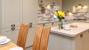 A modern kitchen with grey cabinets, a central island, and a clock on the wall. - Wainwright Lodge (Windermere)