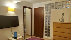 Ein Schlafzimmer mit einem Bett, einer Holzkommode, einem Fernseher und einer Wandleuchte.