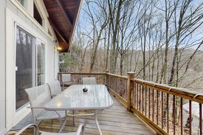 A deck with a glass table and chairs, overlooking a wooded area.