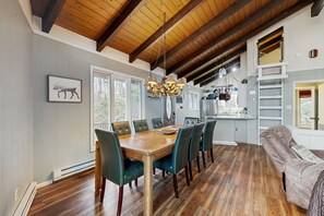 A dining area with a wooden table and chairs, a chandelier, and a view of the kitchen.