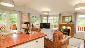 A spacious living room with a wooden coffee table, a brown leather sofa, a television, and a fireplace. - Ambleside Lodge (Windermere)