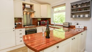 A modern kitchen with white cabinets, a wooden countertop, a stainless steel range hood, a built-in oven, a coffee maker, a toaster, and a window with a view of greenery. - Ambleside Lodge (Windermere)