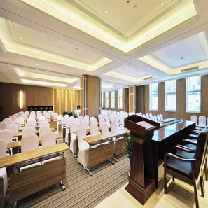 Un salón de conferencias con filas de sillas blancas, un atril y una larga mesa.